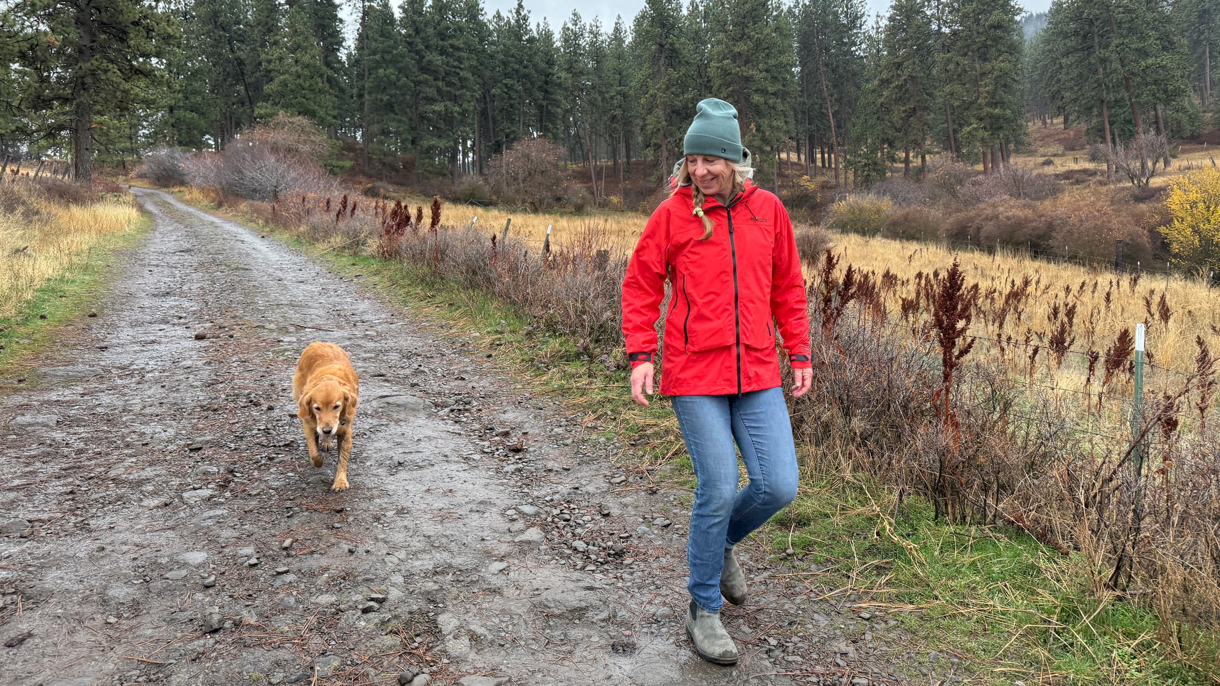 Tester walking with dog down path wearing Columbia Saudan Pro rain shell in wet weather